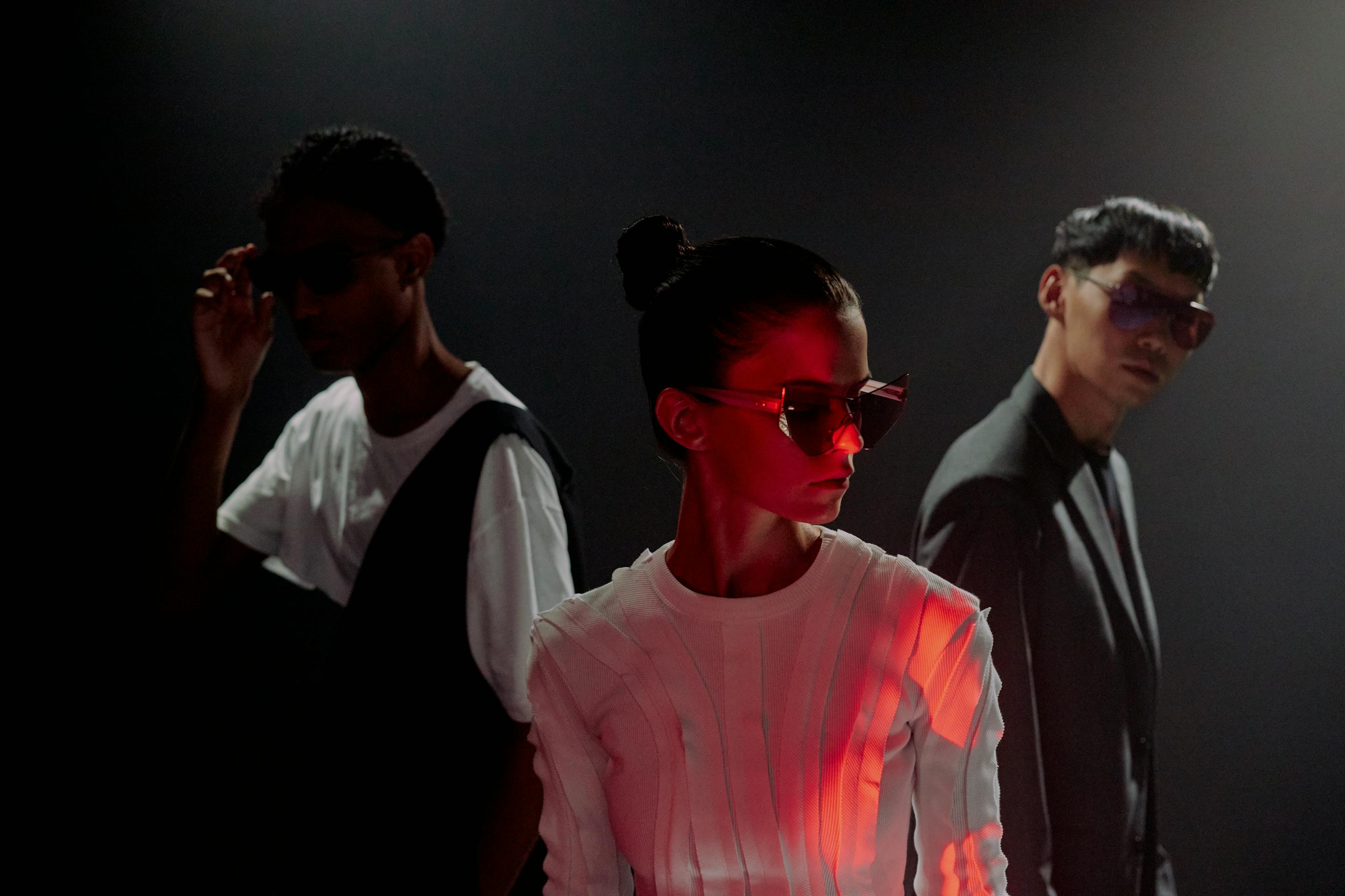 Three people standing in a dark setting with red lighting effects.