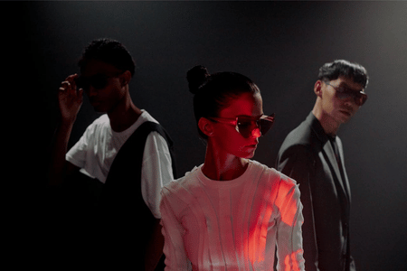 Three people in formal attire with a red light effect on one person against a dark background